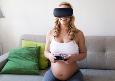 Pregnant woman having fun by playing games and using VR goggles